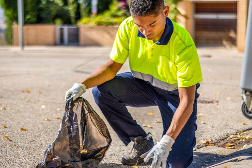 Empleado de limpieza urbana con chaleco reflectante recogiendo basura al aire libre en un día soleado