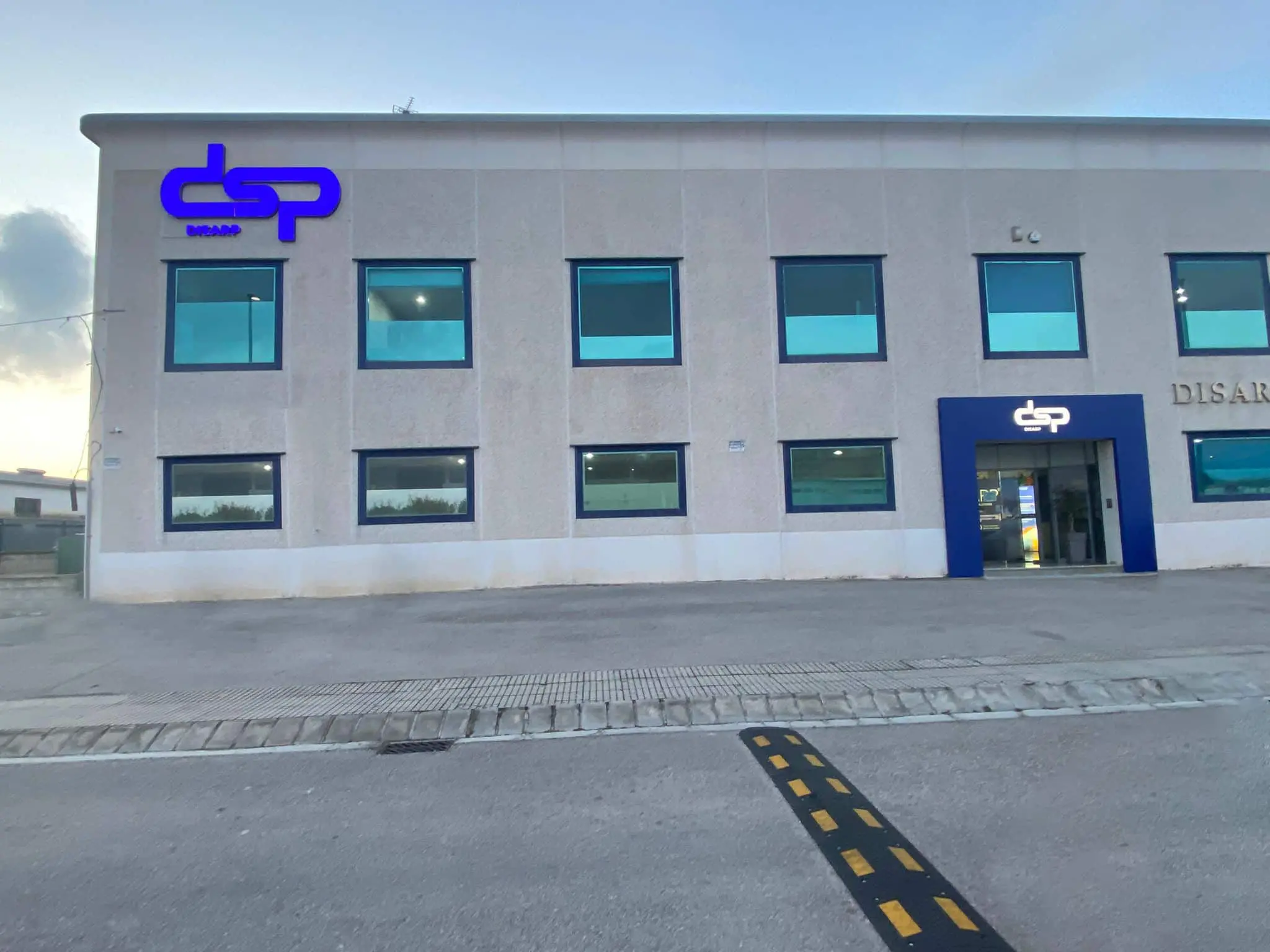 Vista frontal del edificio principal de DSP con fachada clara, ventanas azules y el logotipo corporativo visible en el acceso principal y en la parte superior izquierda del edificio.