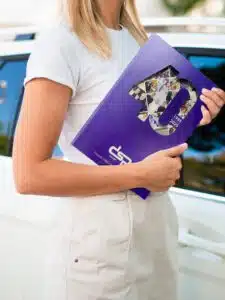 Mujer sosteniendo la revista número 9 de DSP, con portada morada conmemorativa del 40 aniversario (1985–2025), frente a un coche blanco.